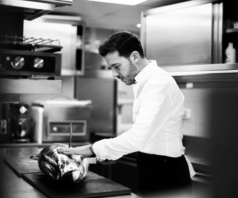 Chef découpant un poisson en cuisine, noir et blanc