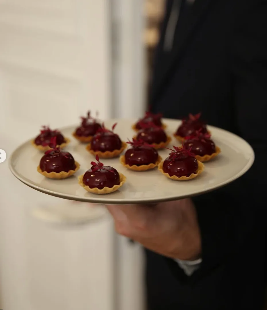 Serveur en costume présentant un plateau de tartelettes rouges