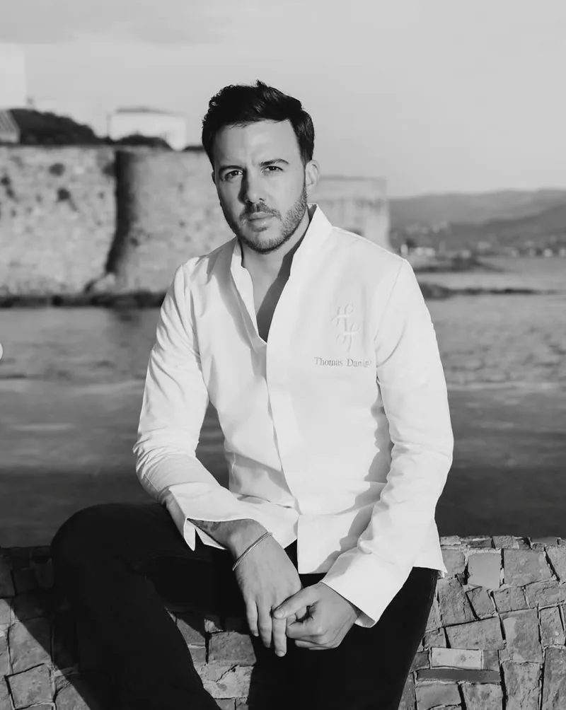 Thomas Danigo debout en bord de mer, veste blanche, noir et blanc