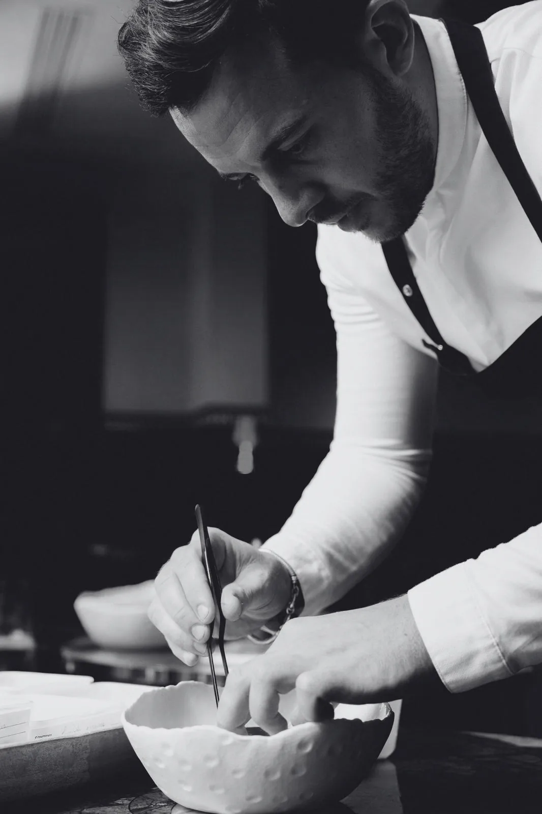 Main de chef dressant une assiette à la pince, en noir et blanc